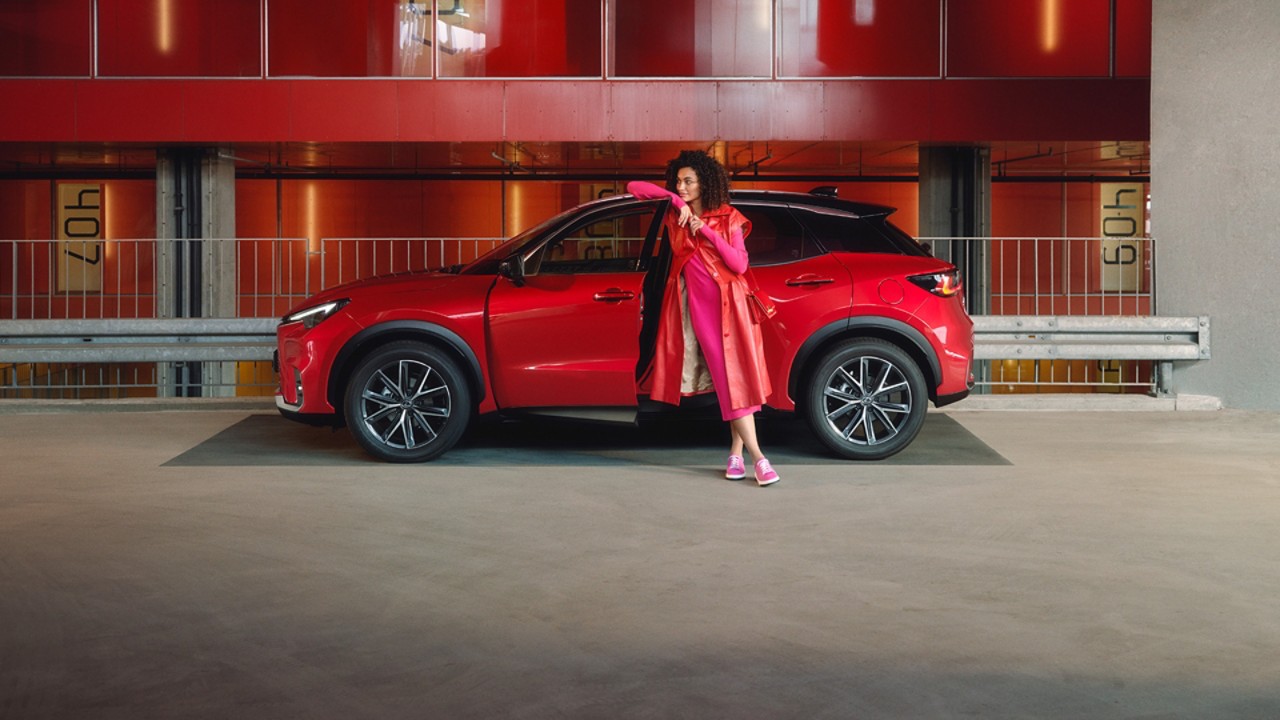 A person leaning against the door of a red Lexus LBX