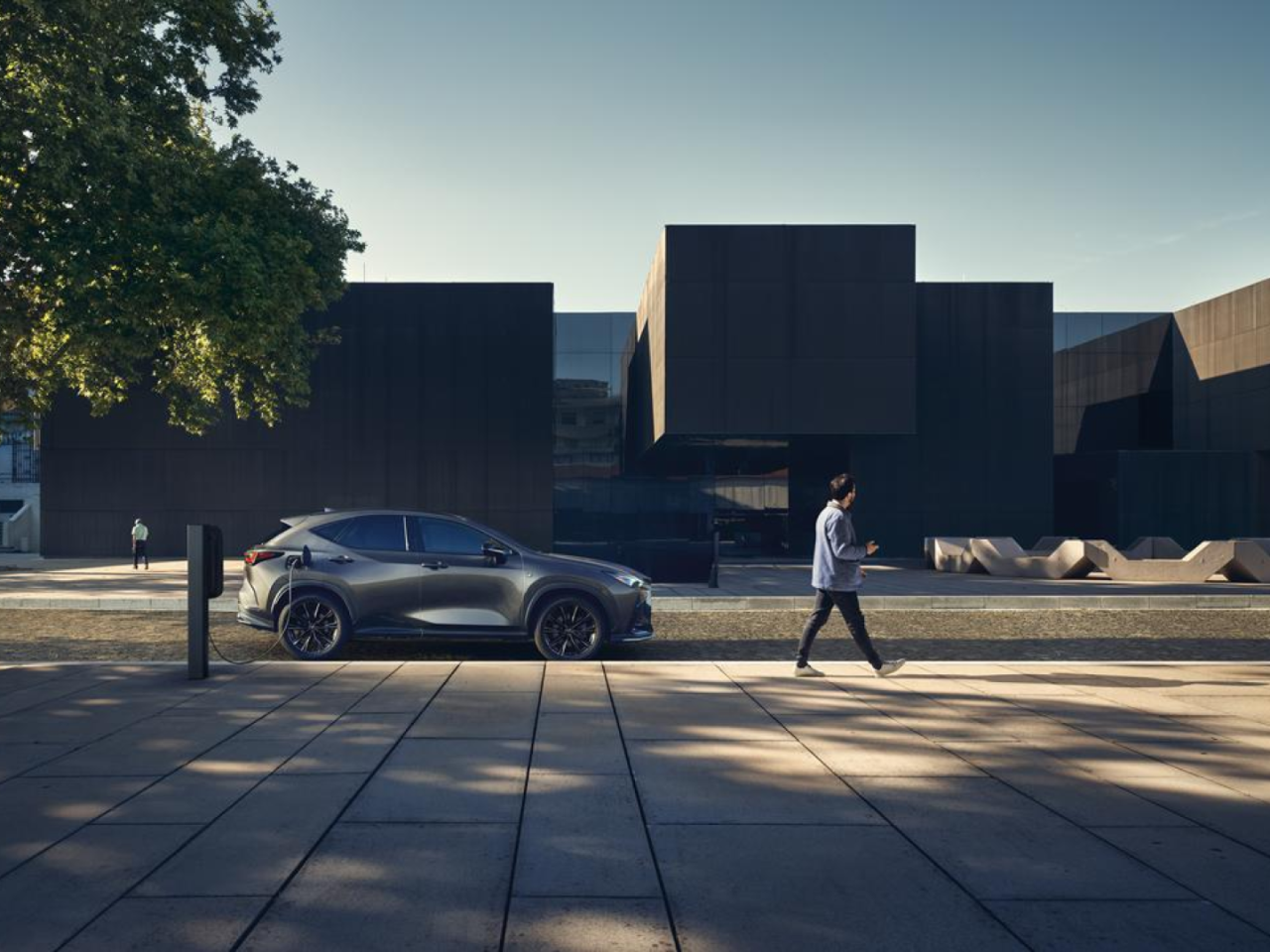 A person walking by a plugged in Lexus NX